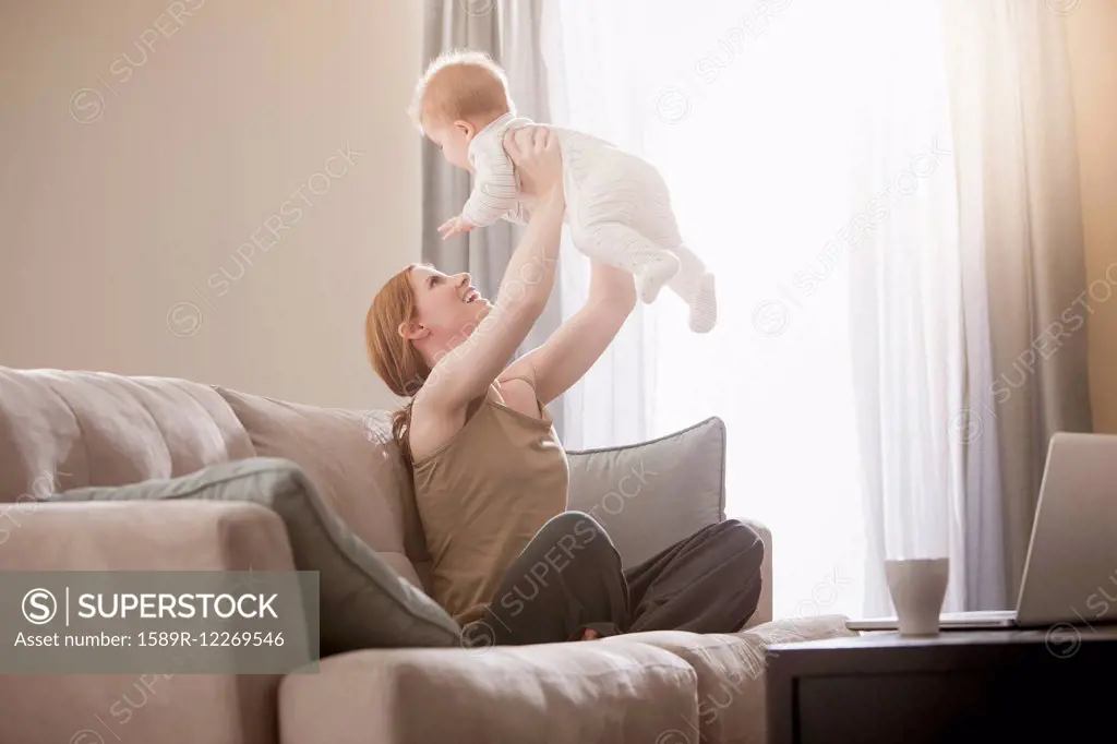 Caucasian mother on sofa lifting son