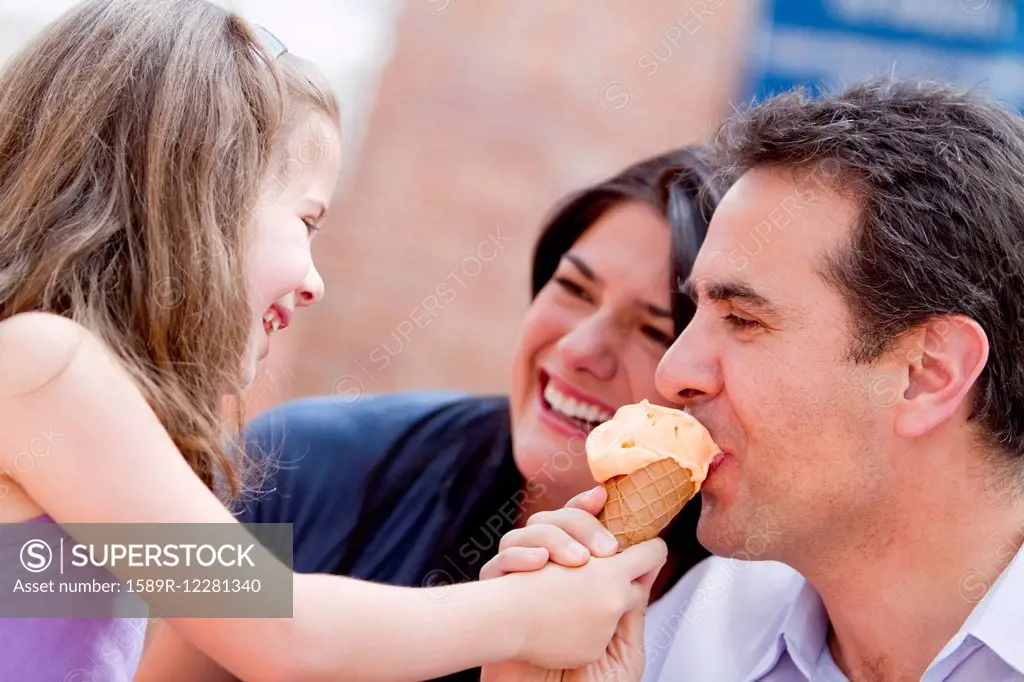 Hispanic girl giving father a bite of her ice cream cone