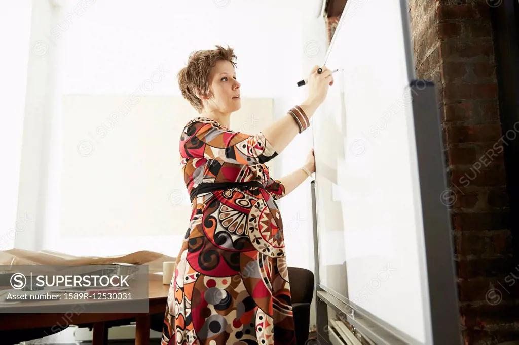 Pregnant businesswoman writing on whiteboard in office
