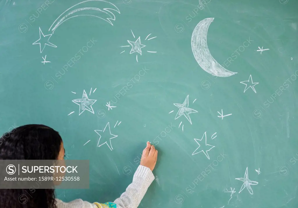 Mixed race student drawing stars on chalkboard in classroom