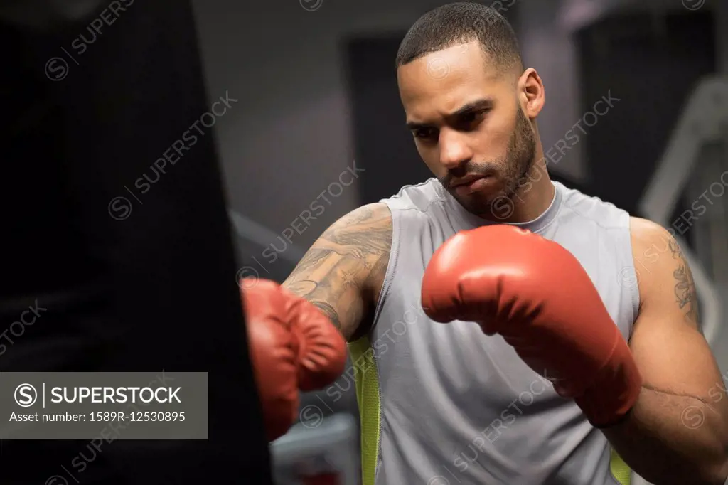Close up of Hispanic man punching bag in gym