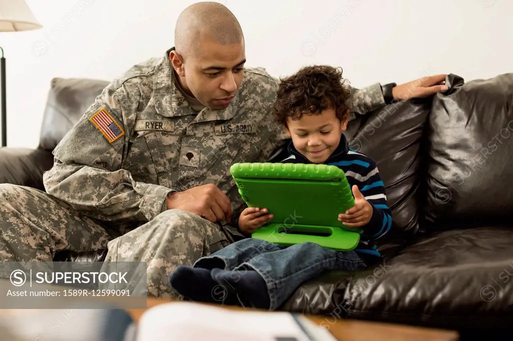 Mixed race soldier father and son using digital tablet on sofa