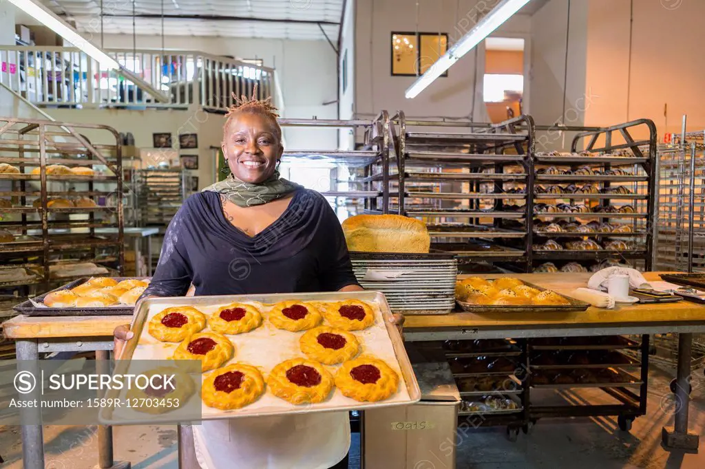 Black baker holding tray of pastries in bakery kitchen