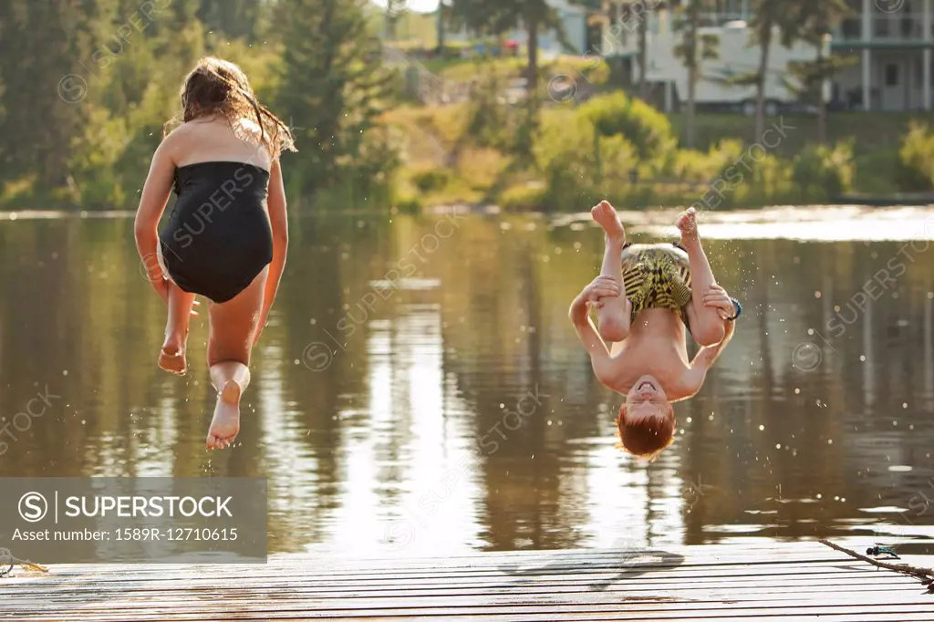 Caucasian children jumping into lake