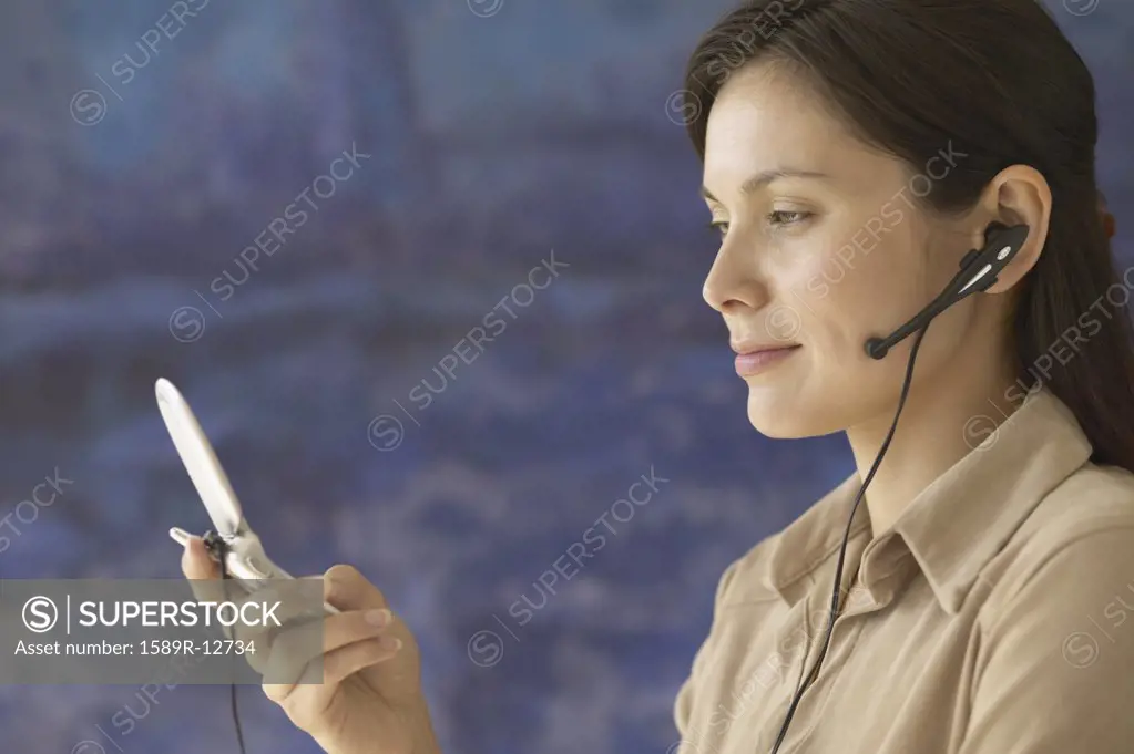 Side view of woman holding cell phone with earpiece