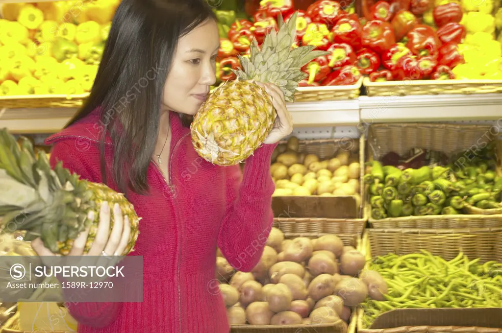 Young woman smelling a pineapple in a supermarket
