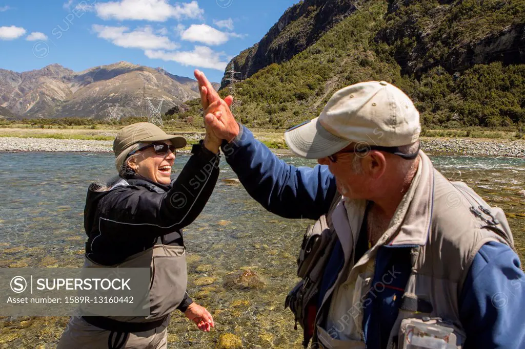 Caucasian couple high-fiving in remote river