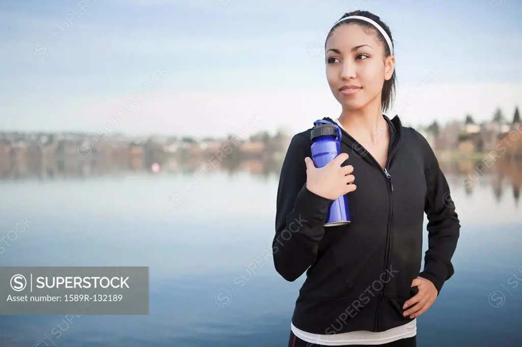 Mixed race woman near lake holding water bottle