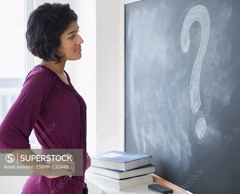 Hispanic woman looking at question mark on blackboard