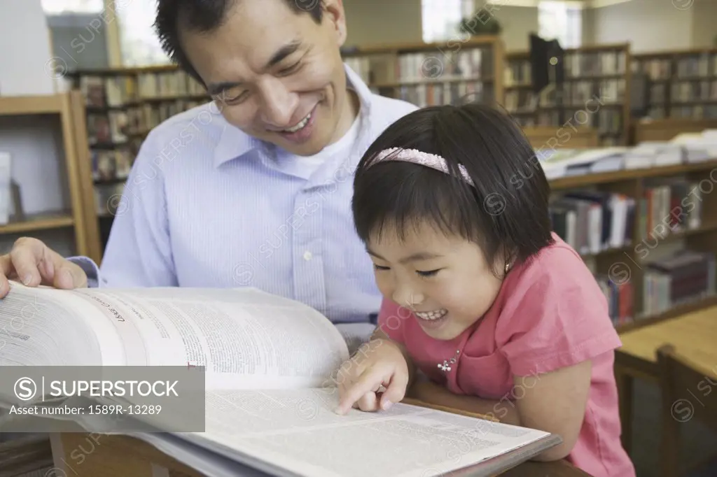 Father and daughter reading books in library
