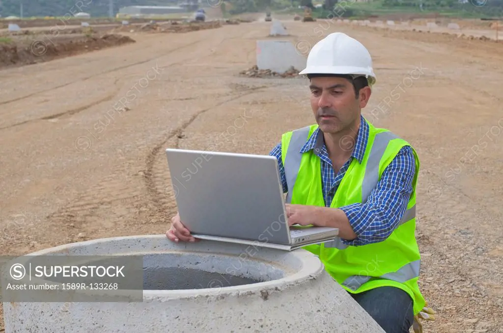 Hispanic construction worker using laptop in field