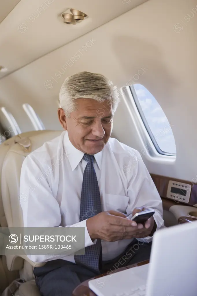 Hispanic businessman using cell phone on private jet
