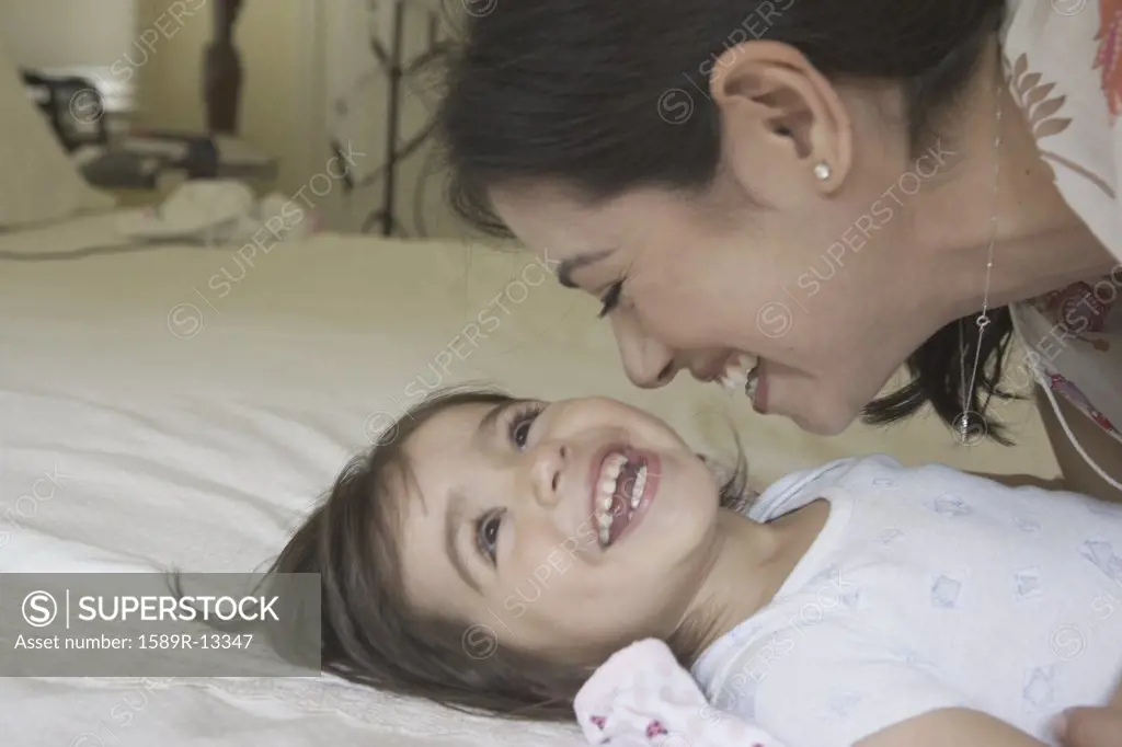 Mother playing with toddler girl on the bed