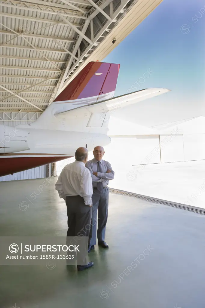 Hispanic businessmen standing in airplane hangar