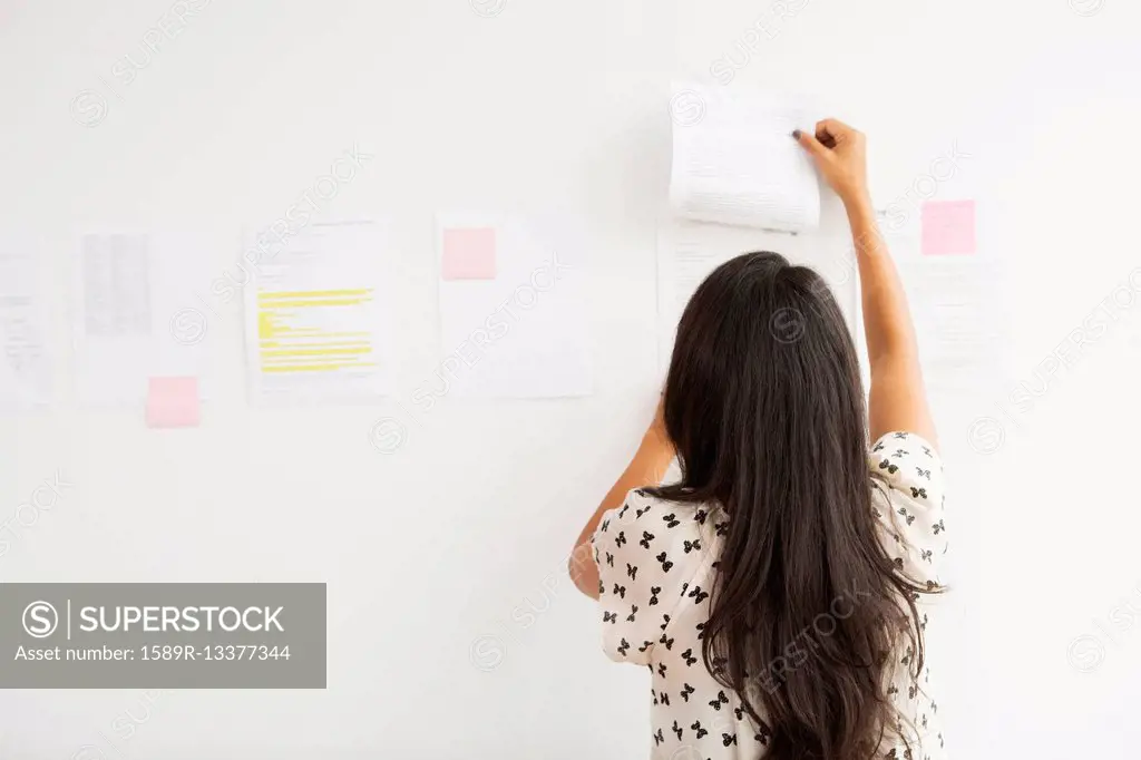 Businesswoman taping up papers on office wall