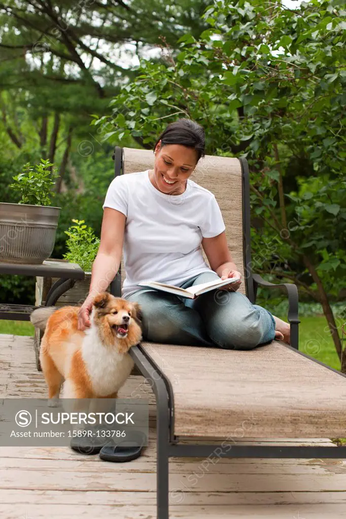 African American woman reading book and petting dog