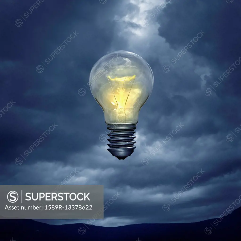 Illuminated light bulb floating in stormy sky