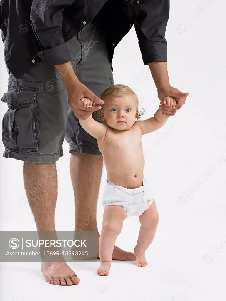 Mixed race father helping baby girl learn to walk