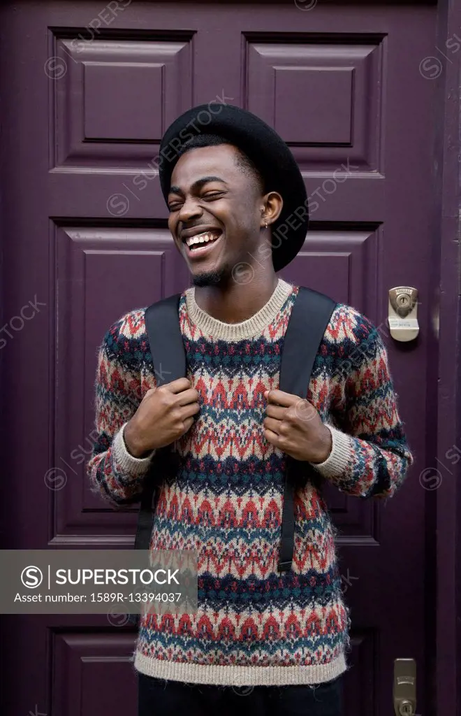 Laughing Black man wearing backpack near purple door