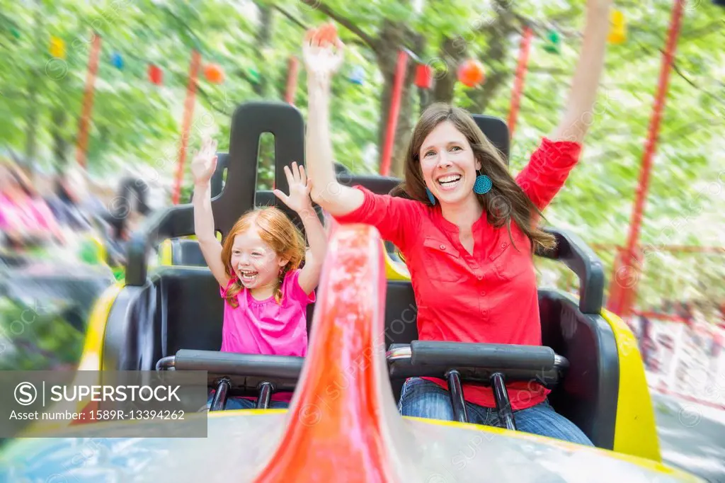 Mother and daughter riding roller coaster in amusement park