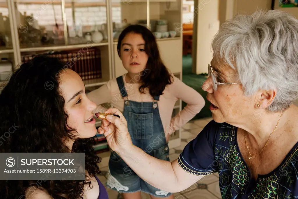 Grandmother applying lipstick to granddaughter in dining room