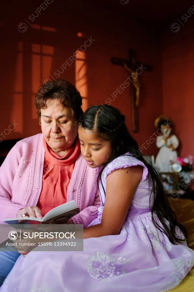 Hispanic grandmother and granddaughter ready book on bed