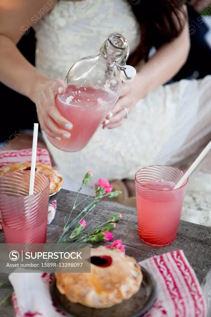 Woman pouring pink lemonade into glasses on wooden table