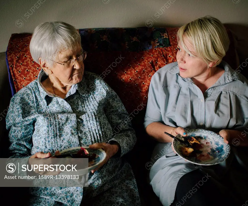 Older woman and granddaughter eating on sofa