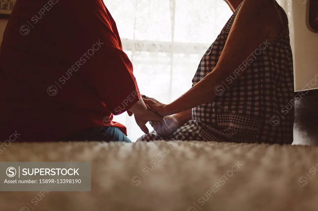 Older woman holding hand of daughter on bed