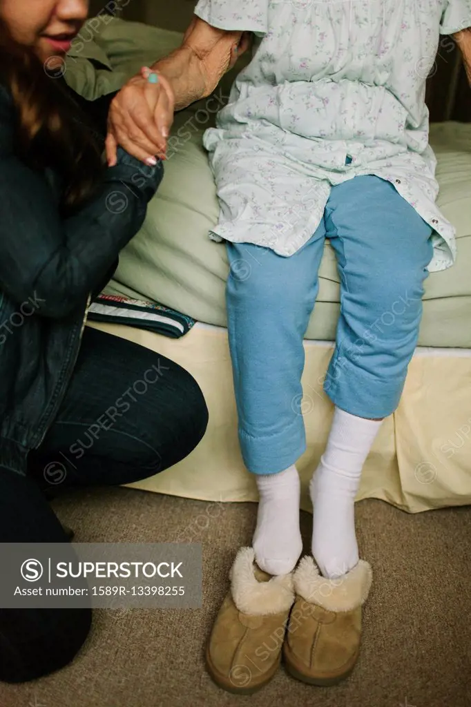 Granddaughter helping grandmother out of bed into slippers
