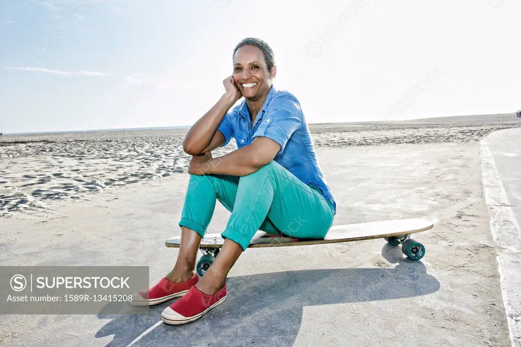 Older Black woman sitting on skateboard on beach