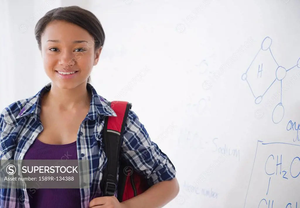 Smiling mixed race teenage girl standing next to whiteboard in science class
