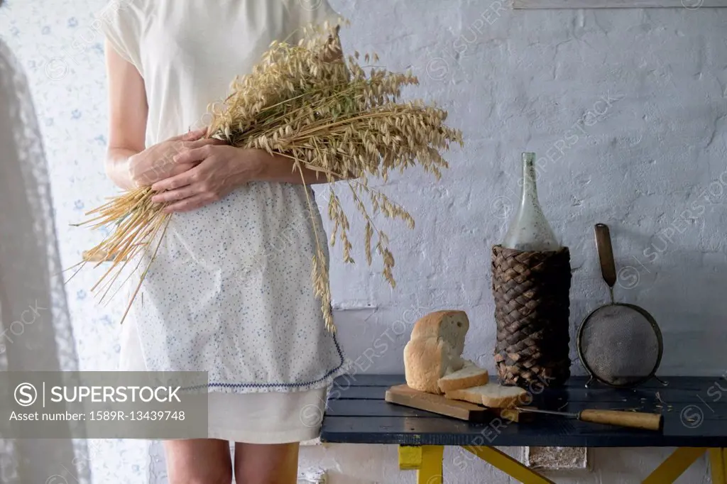 Caucasian woman holding bouquet of wheat near sliced bread