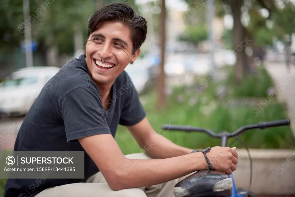 Laughing Hispanic man sitting with bicycle