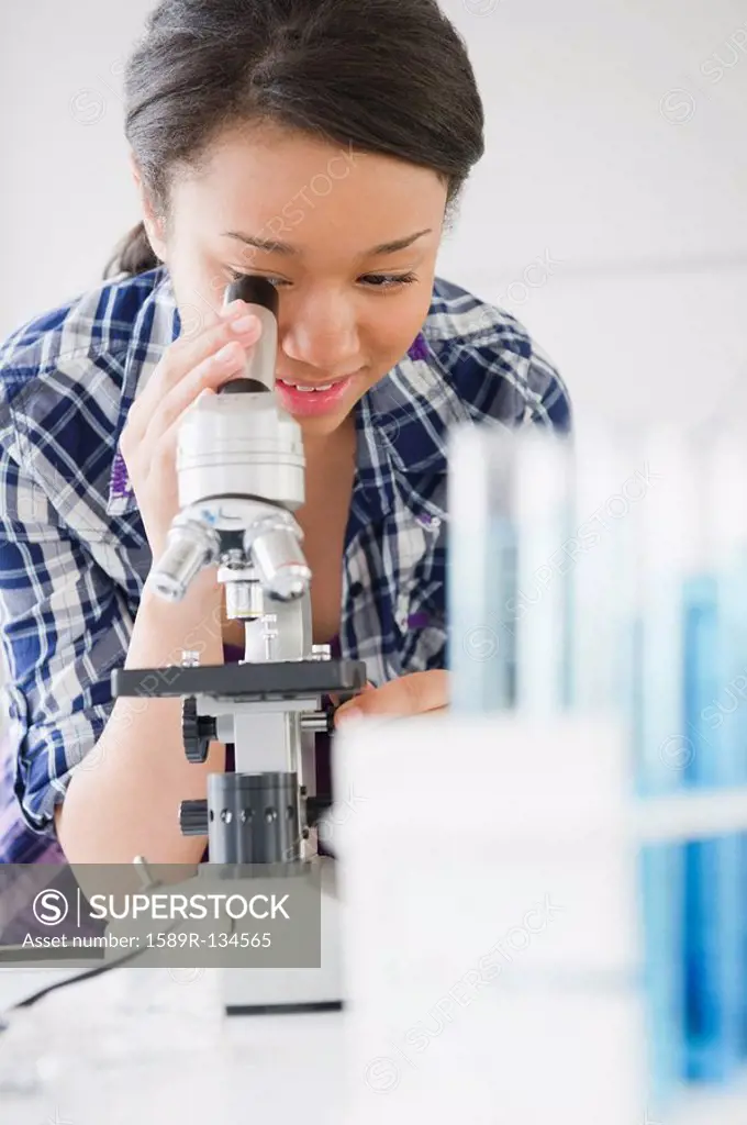 Mixed race teenage girl looking through microscope