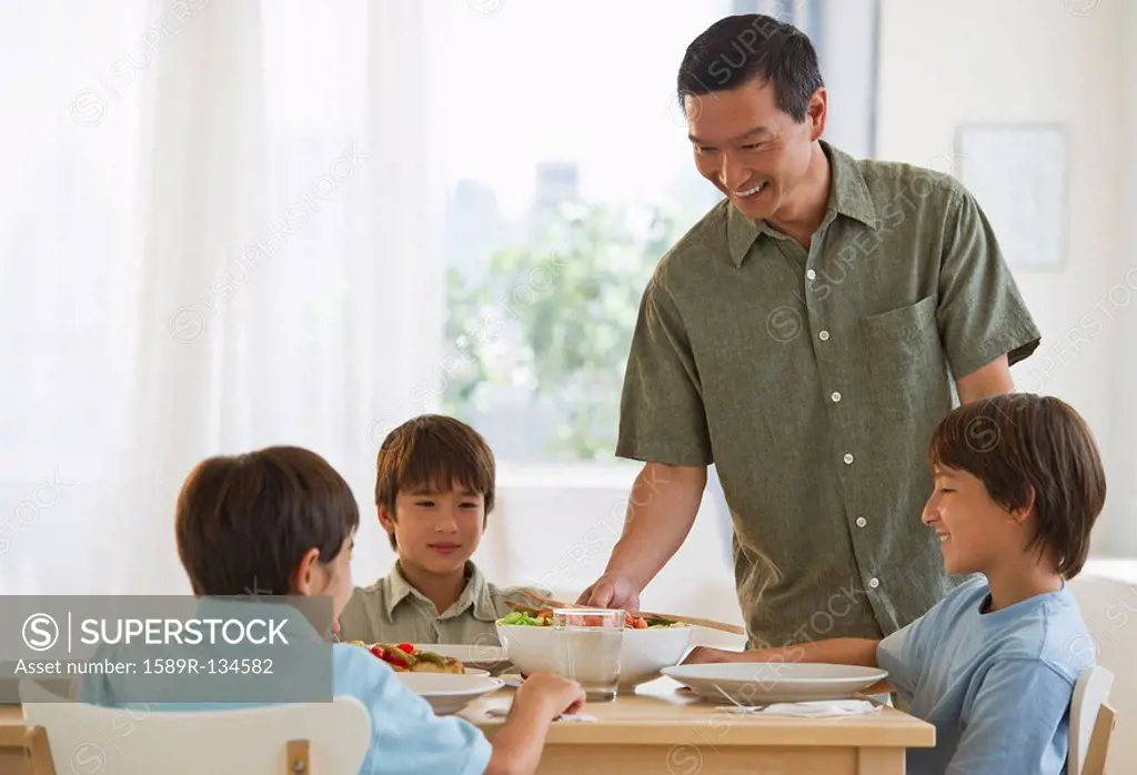Father serving dinner to sons at table