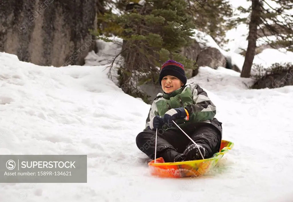 Smiling Hispanic boy riding sled in snow