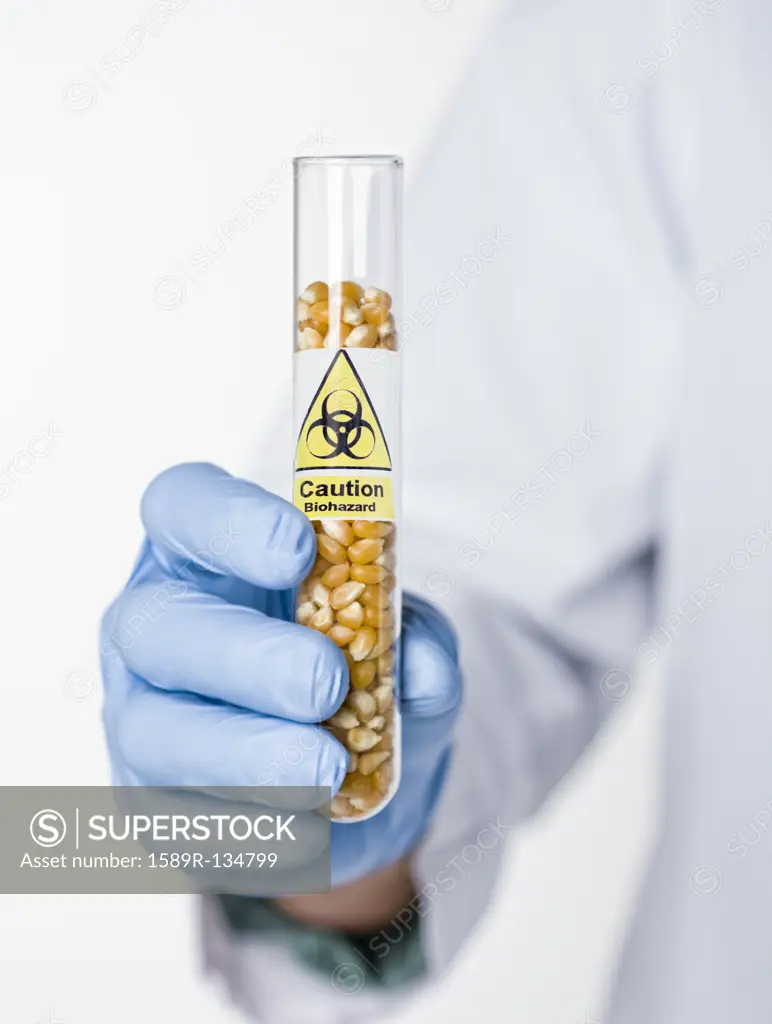 Hispanic scientist holding test tube with caution symbol containing