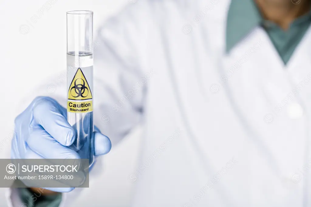 Hispanic scientist holding test tube with caution sticker full of water