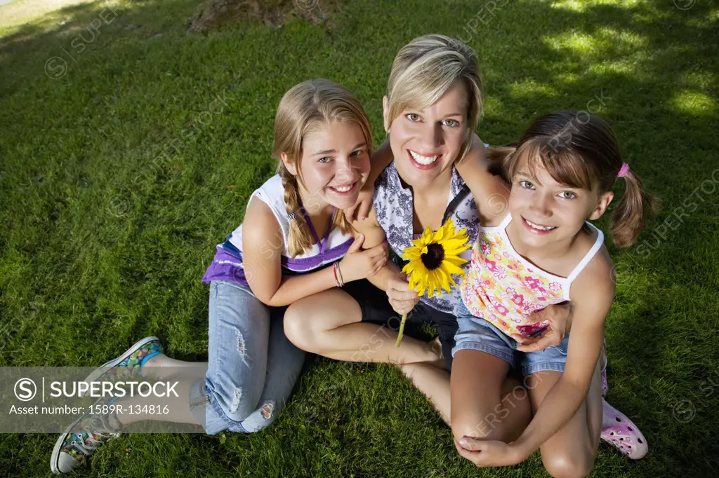 Caucasian mother and daughters sitting grass