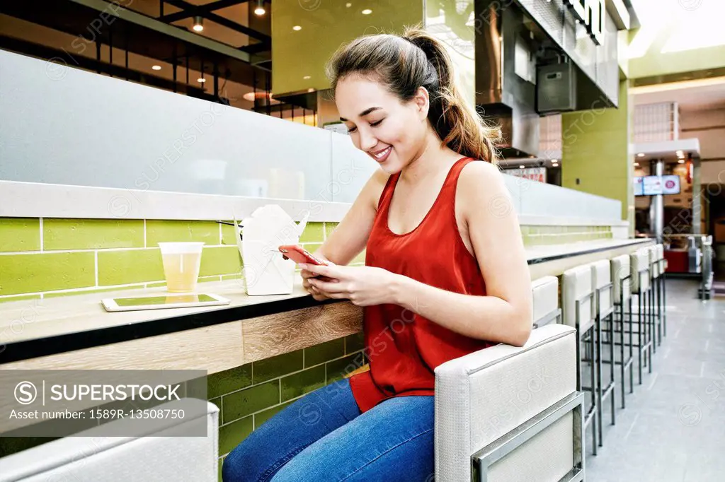 Mixed Race woman in food court texting on cell phone