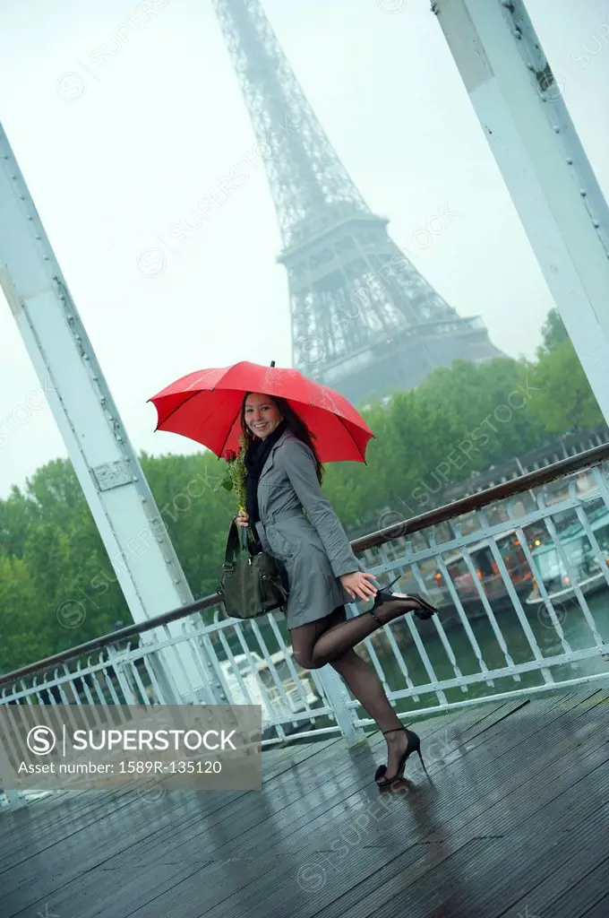 Caucasian woman in high heel shoes with red umbrella near Eiffel Tower