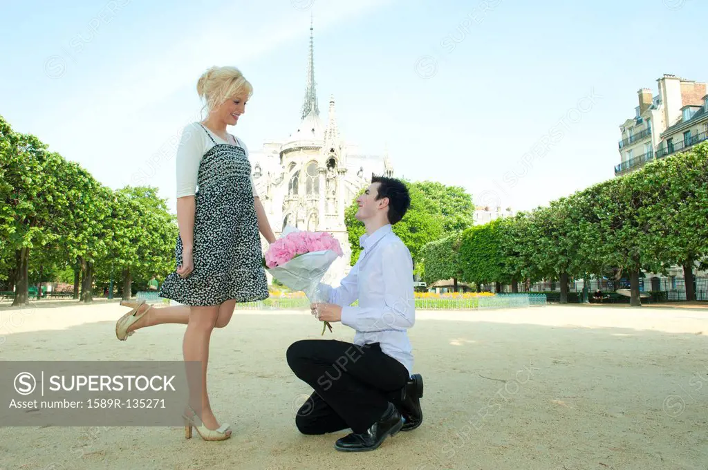 Caucasian man proposing to girlfriend in park near Notre Dame