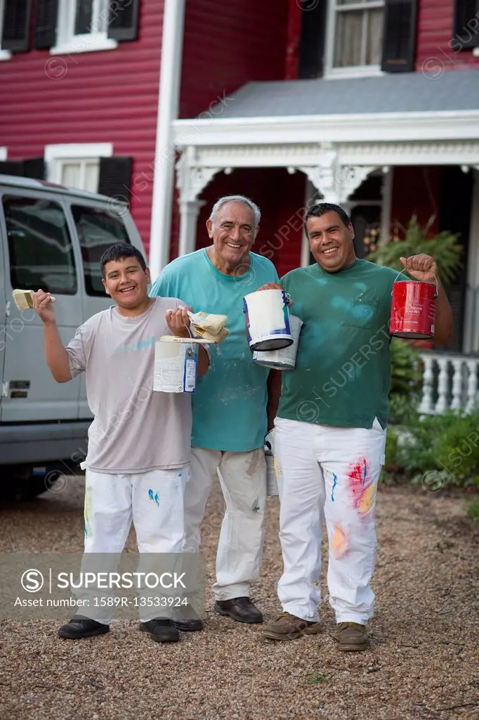 Smiling Hispanic men and boy posing with paint cans and paintbrushes