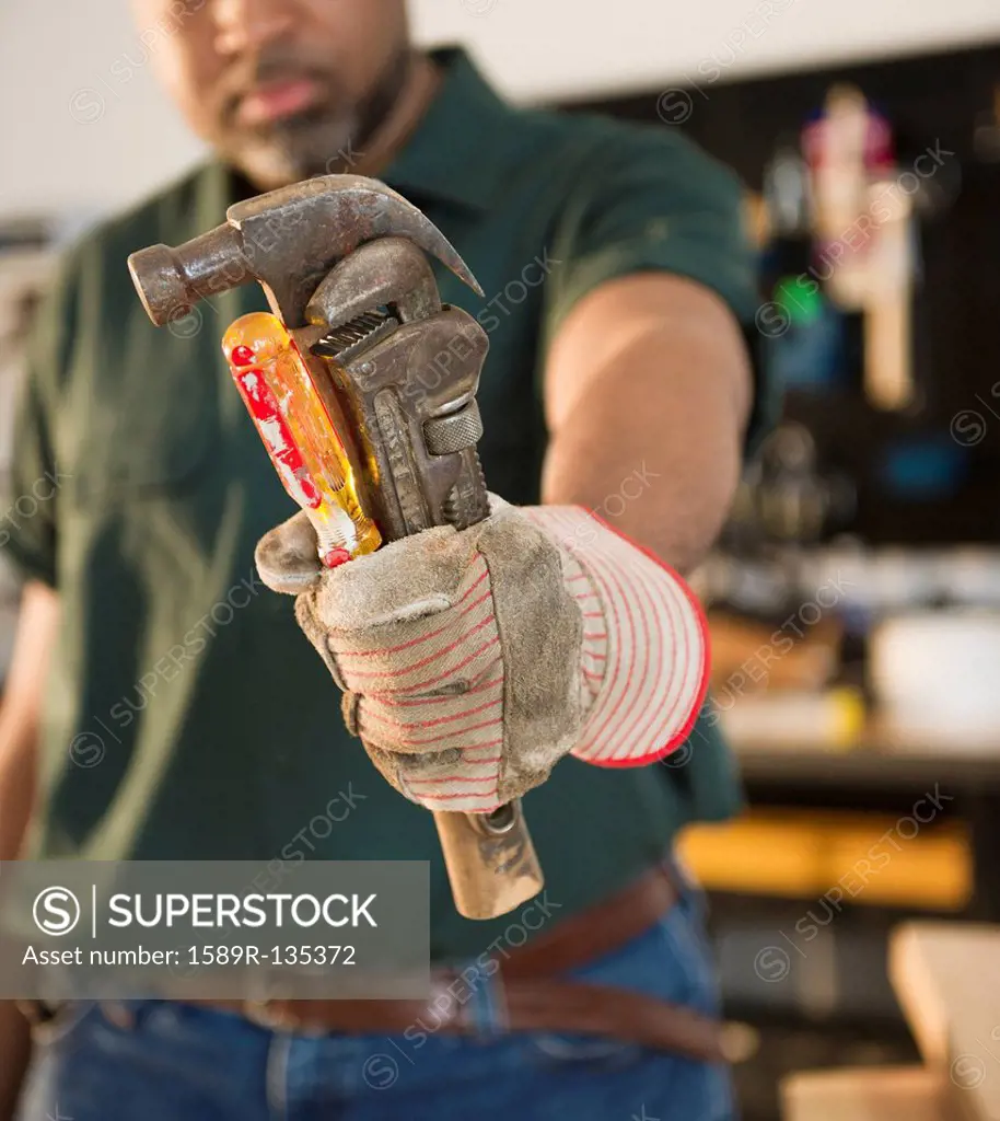 African American carpenter holding screwdriver, wrench and hammer