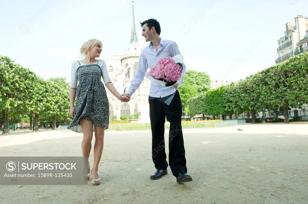 Caucasian couple holding hands in park near Notre Dame