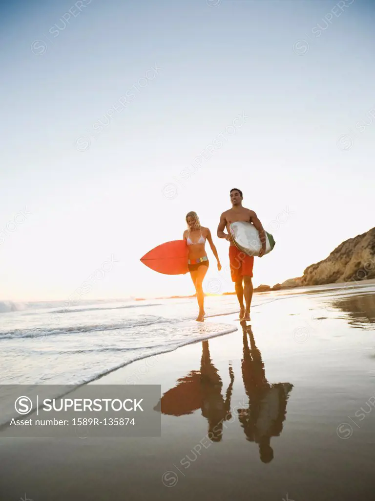 Couple walking on beach carrying surfboards