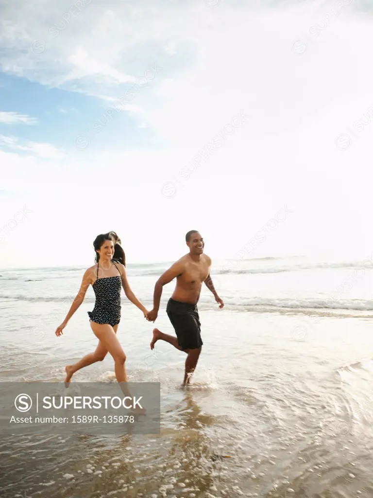 Couple holding hands and running on beach