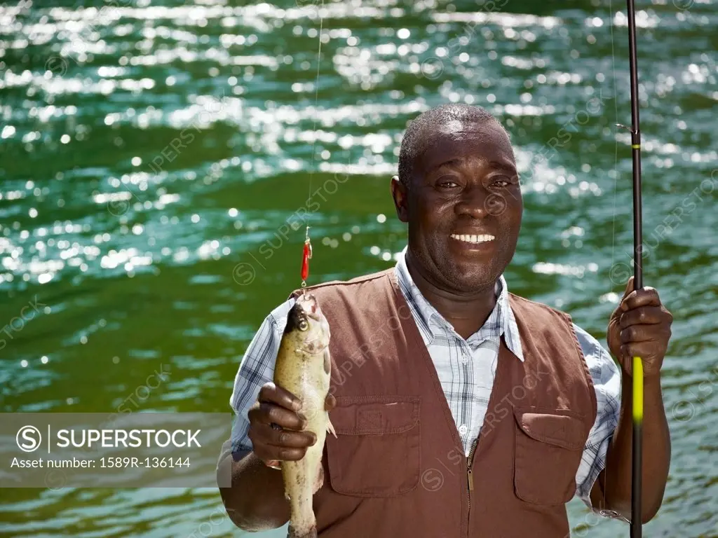 Black man holding fish and fishing rod near stream
