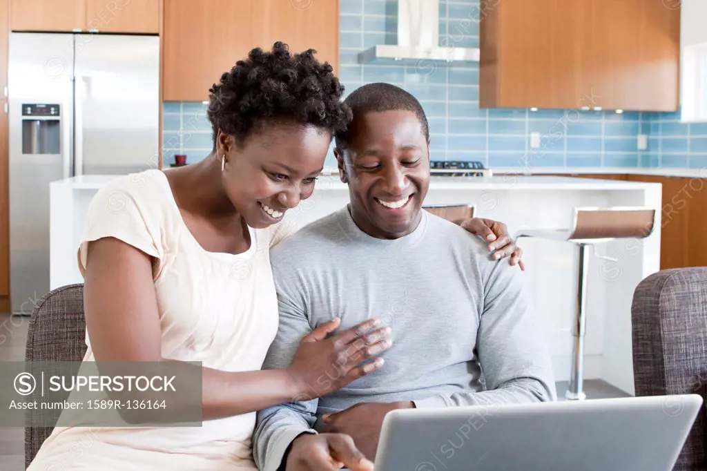 Black couple hugging and using laptop